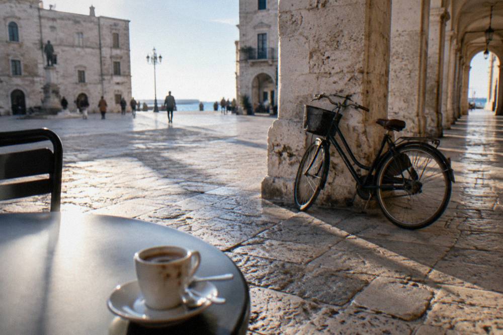 Worn limestone paving beside loggia arches with a leaning bicycle and an espresso cup on a small round table