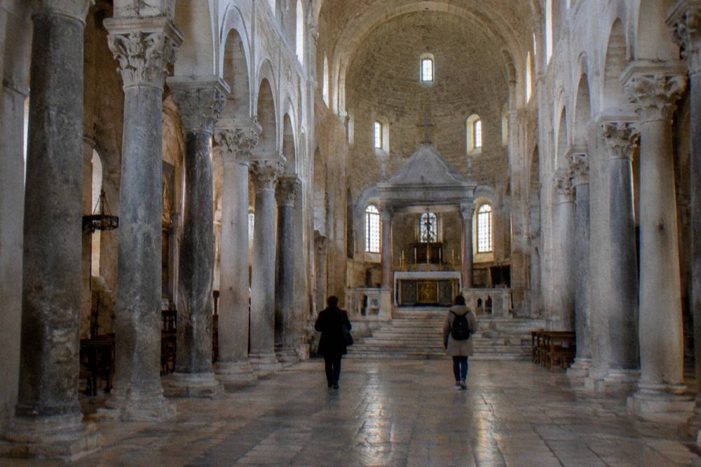 Long stone nave of a Romanesque basilica with simple columns and a raised sanctuary in soft window light