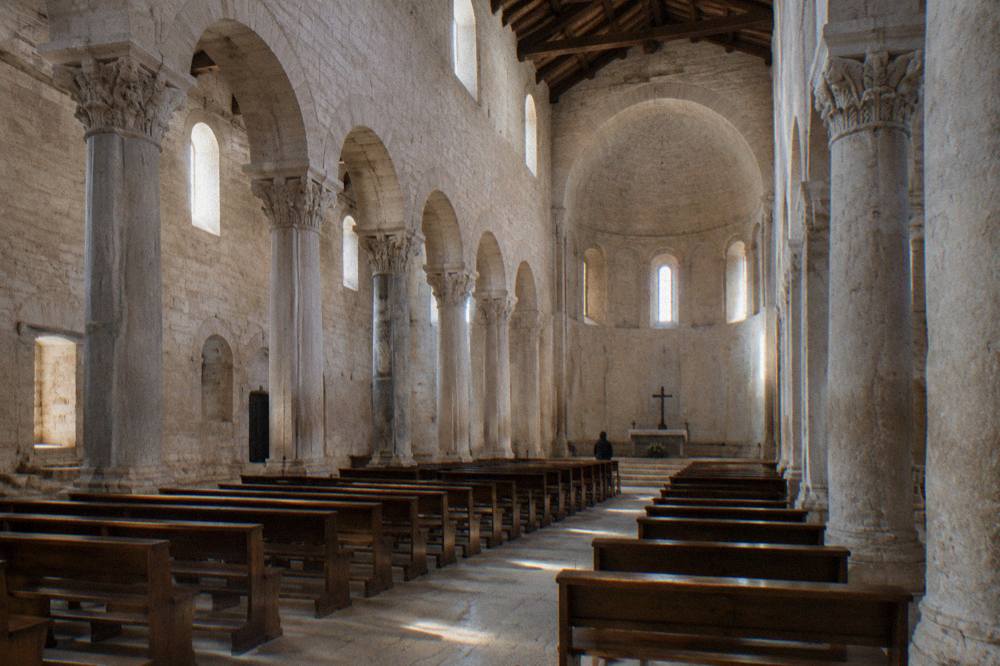 Bare stone cathedral interior with round arches, a high apse and shafts of light from small windows