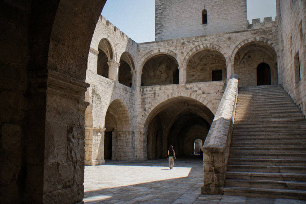 Inner courtyard of a medieval castle with a pale stone arcade, a broad staircase and a vaulted passage