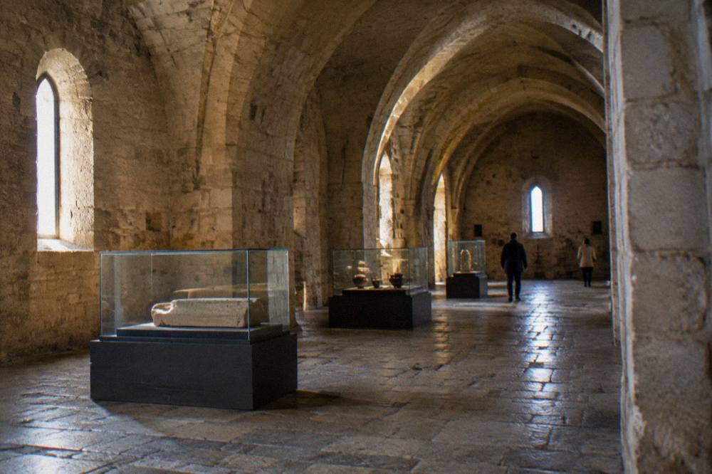 Vaulted stone hall inside a castle with plain exhibition cases and a worn flagstone floor