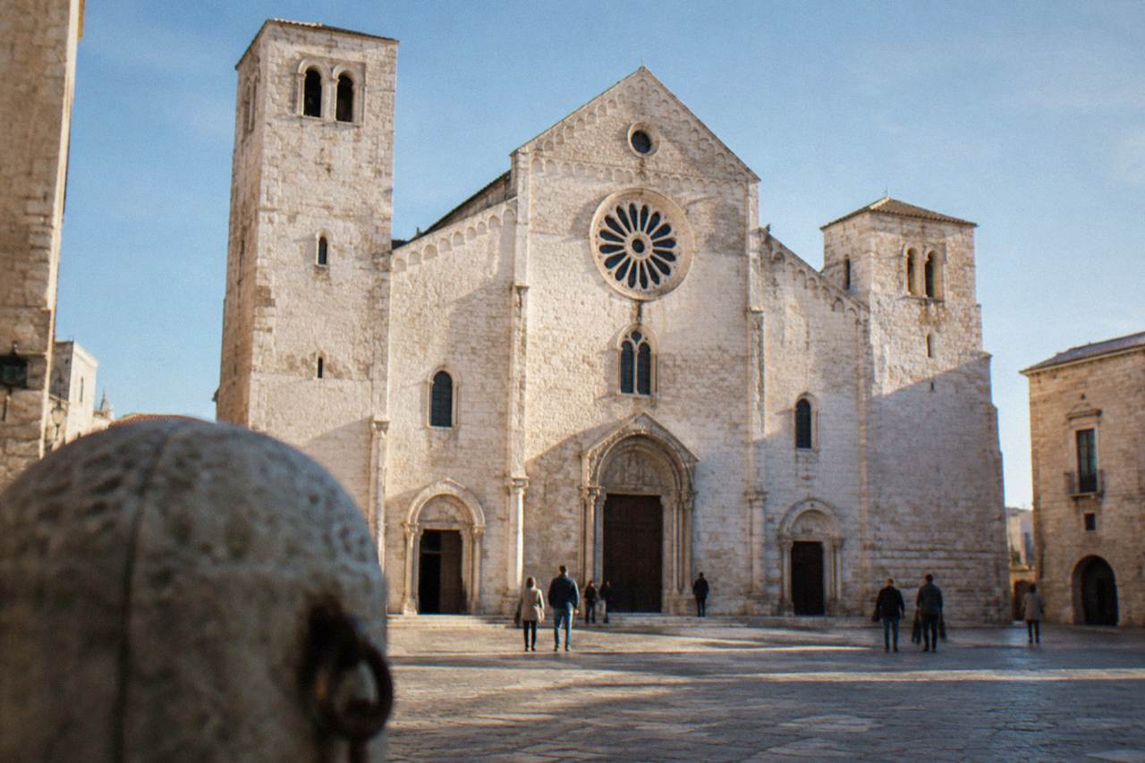 Romanesque church of pale limestone with a wide plain facade, two squat towers and a rose window above a paved square