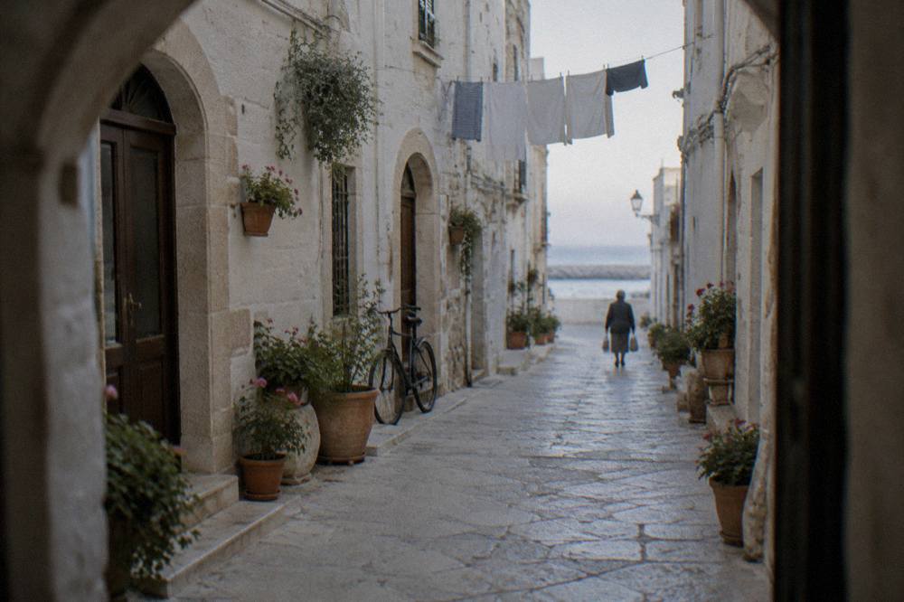 Narrow whitewashed old town lane with arched doorways, flower pots, washing overhead and a leaning bicycle in soft morning light