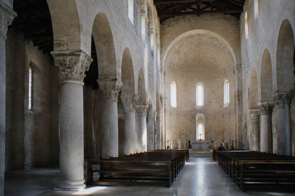 Bare stone cathedral interior with round arches, a high apse and shafts of light from small windows