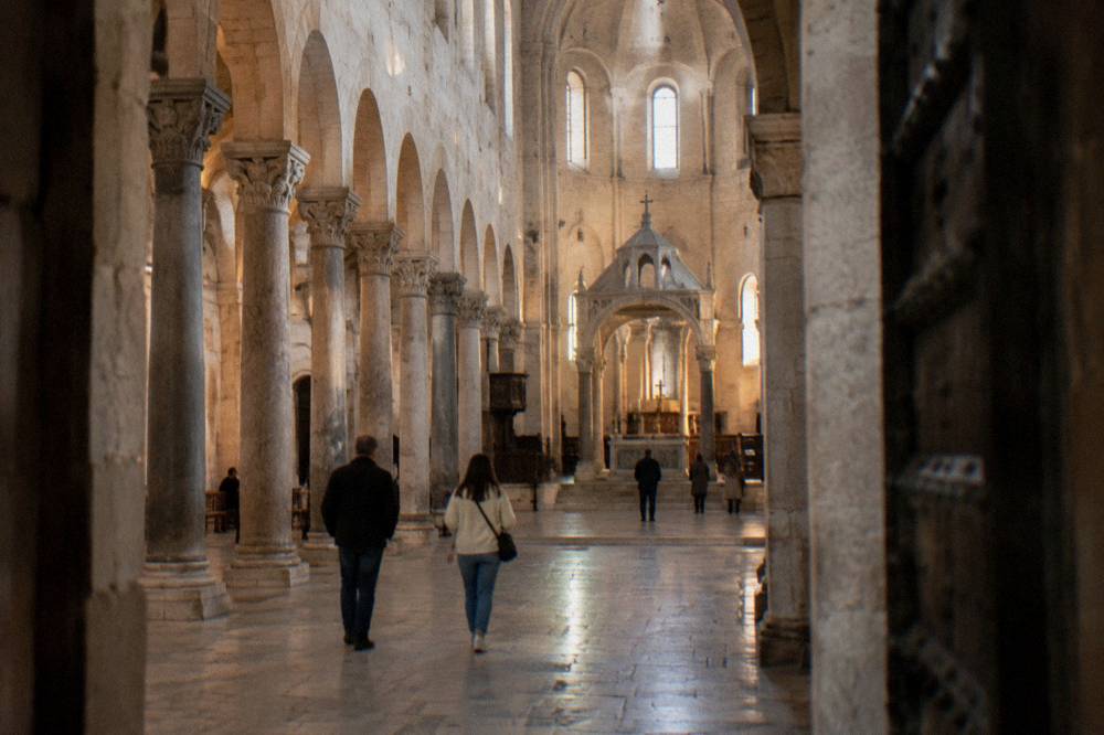 Long stone nave of a Romanesque basilica with simple columns and a raised sanctuary in soft window light