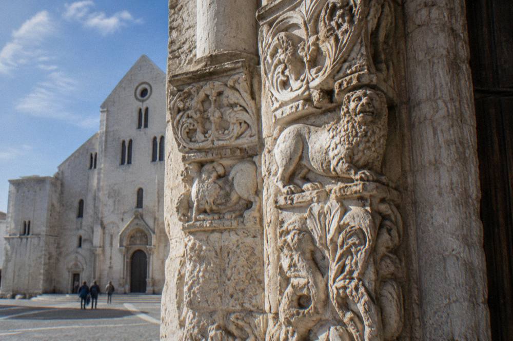 Weathered pale limestone carving of animals and foliage around a Romanesque church doorway in soft side light