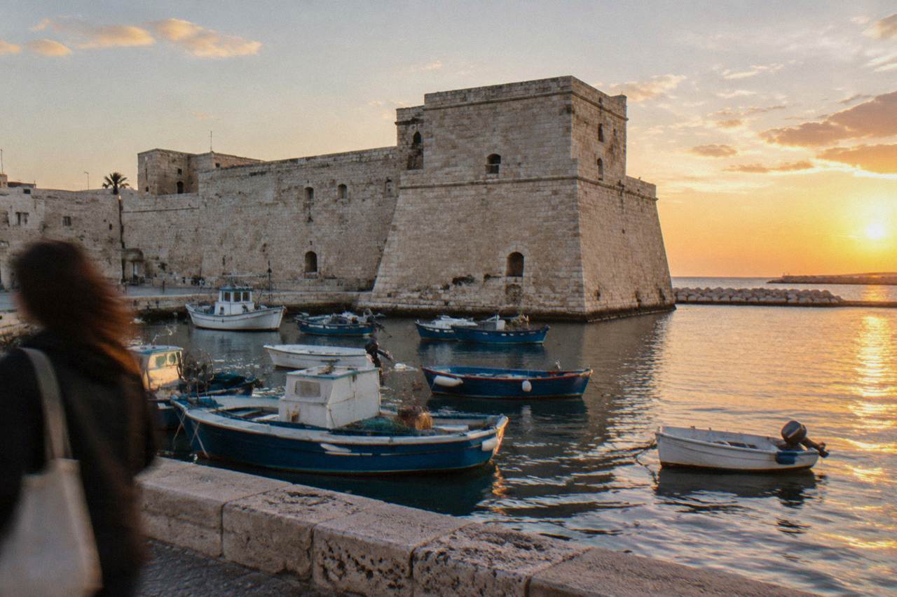 Squat pale limestone fort with thick sloping walls at the edge of the old harbour with small fishing boats moored in front