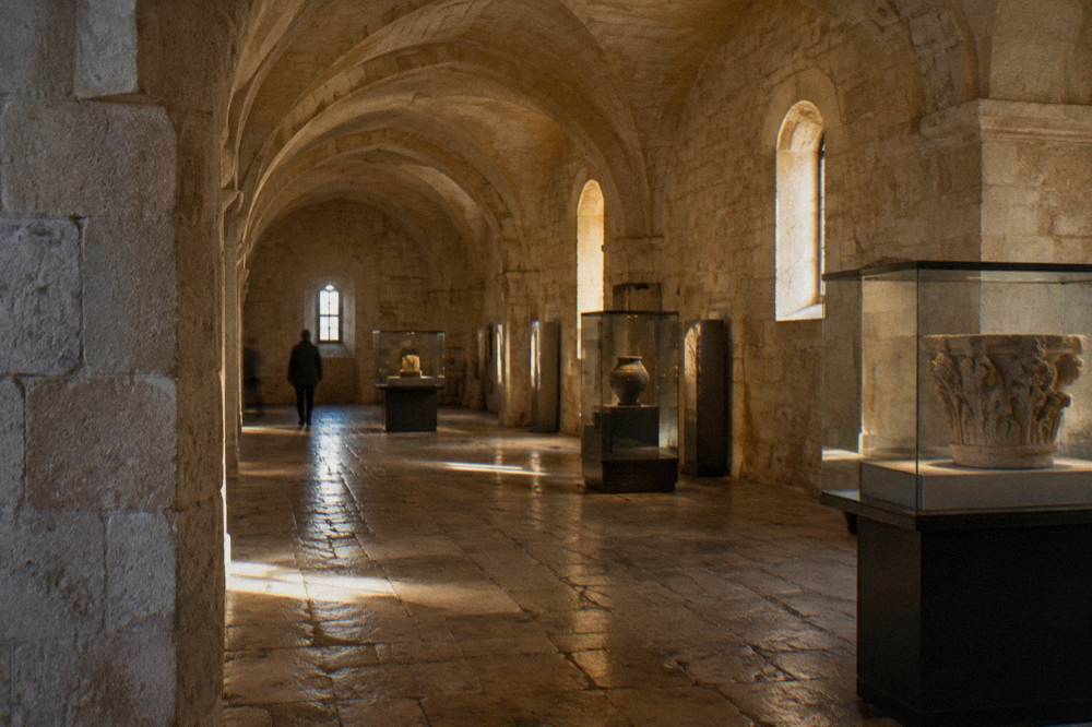 Vaulted stone hall inside a castle with plain exhibition cases and a worn flagstone floor