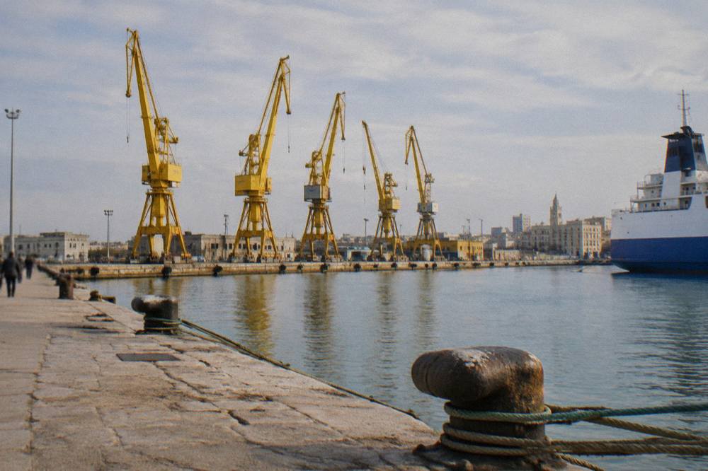 Row of harbour cranes behind a calm commercial dock with ropes and bollards in the foreground