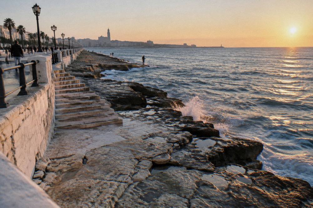 Stone steps down to flat limestone rocks below a sea wall with distant anglers fishing and light sea spray