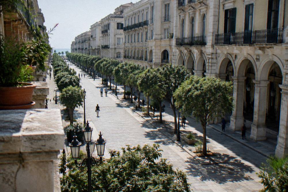Long straight tree-lined boulevard of neoclassical buildings with arcaded ground floors