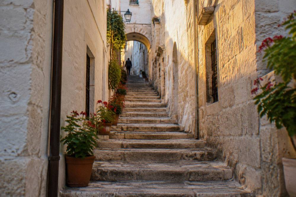 Narrow lane with a steep stone staircase climbing between whitewashed walls to a small arch with potted geraniums