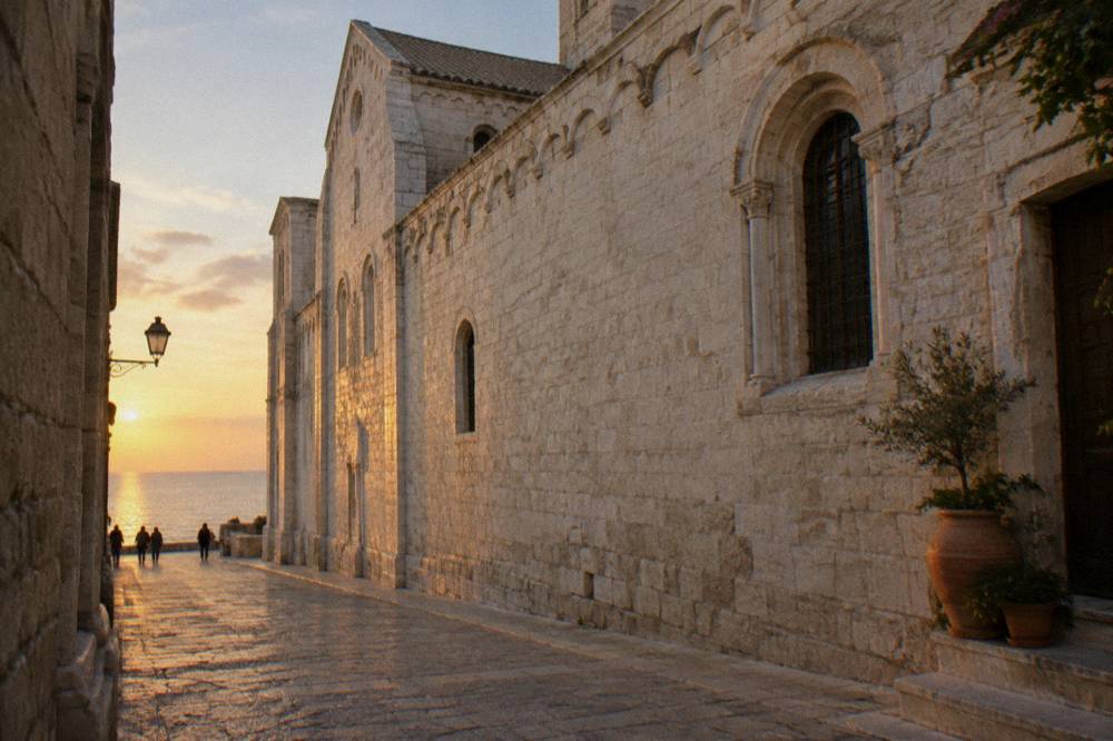 Long pale limestone flank of a Romanesque church seen from a narrow old-town lane with pots on a doorstep