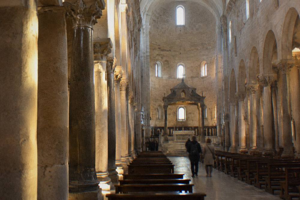 Long stone nave of a Romanesque basilica with simple columns and a raised sanctuary in soft window light