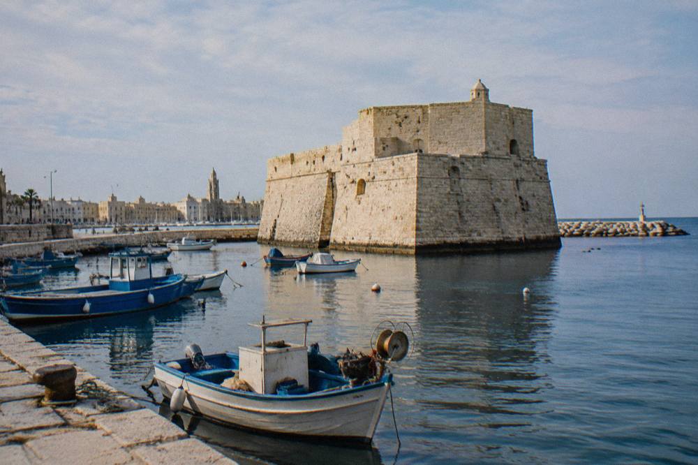 Squat pale limestone fort with thick sloping walls at the edge of the old harbour with small fishing boats moored in front