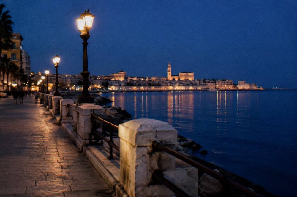 Seafront promenade at blue hour with lit street lamps and the lights of the old town across the bay