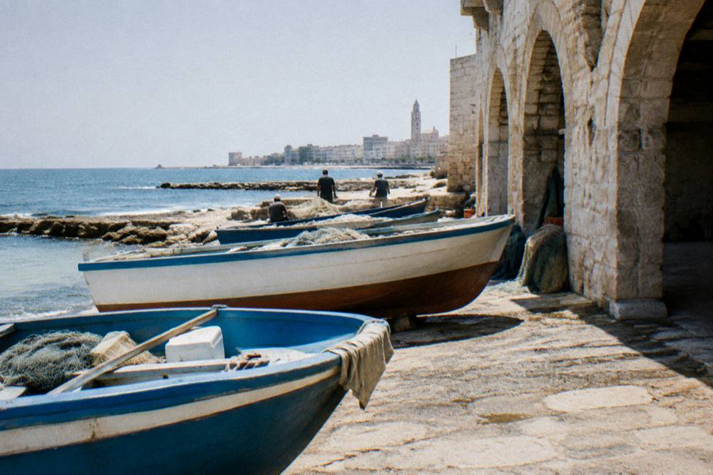 Small rowing boats on a stone slipway with distant fishermen mending nets in soft light