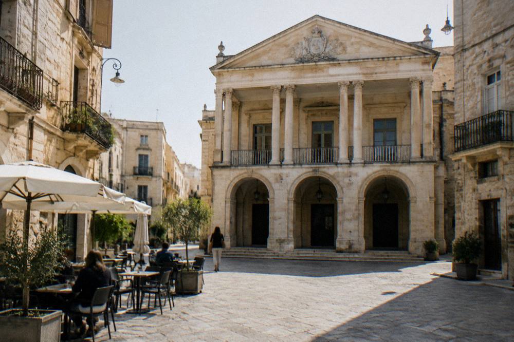 Small neoclassical theatre facade with a pediment and slim columns on a narrow old town square