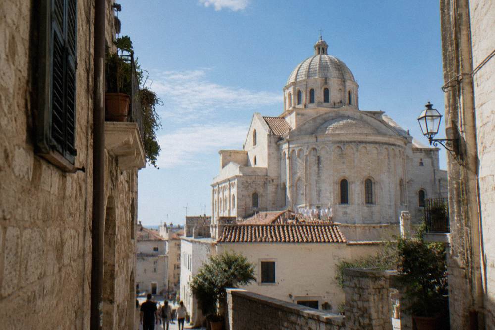 Cathedral dome and apse rising above terracotta rooftops at the end of a narrow old-town lane in afternoon light