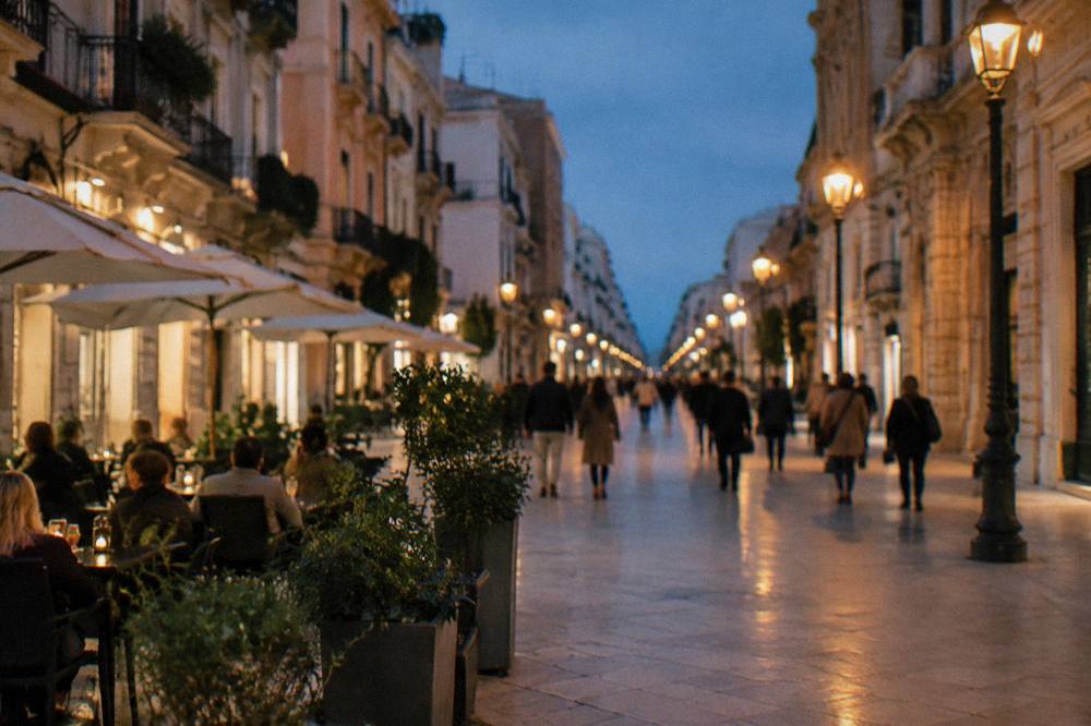 Pedestrian shopping street in the evening with lit lamps, cafe tables and out-of-focus people