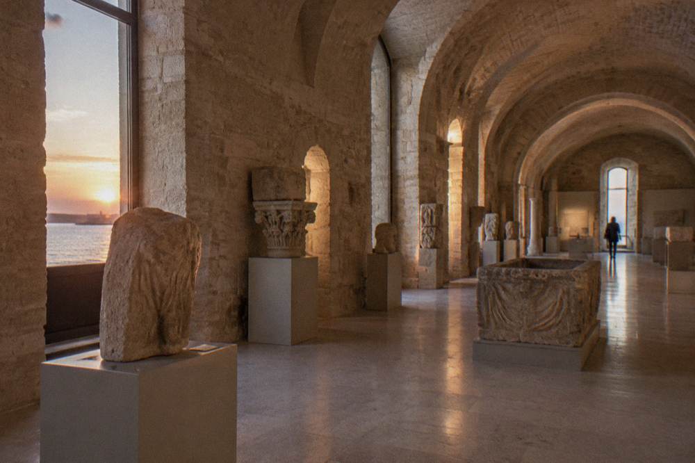 Vaulted stone hall with archaeological finds on plain plinths in soft light