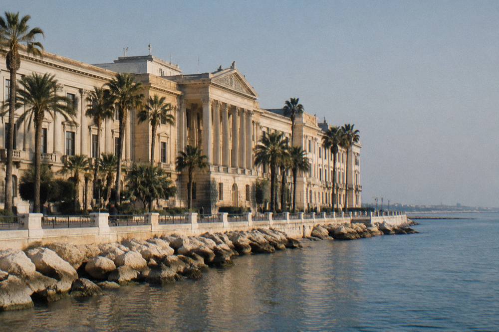 Grand neoclassical seafront palace with a long cream facade, a central portico and palm trees