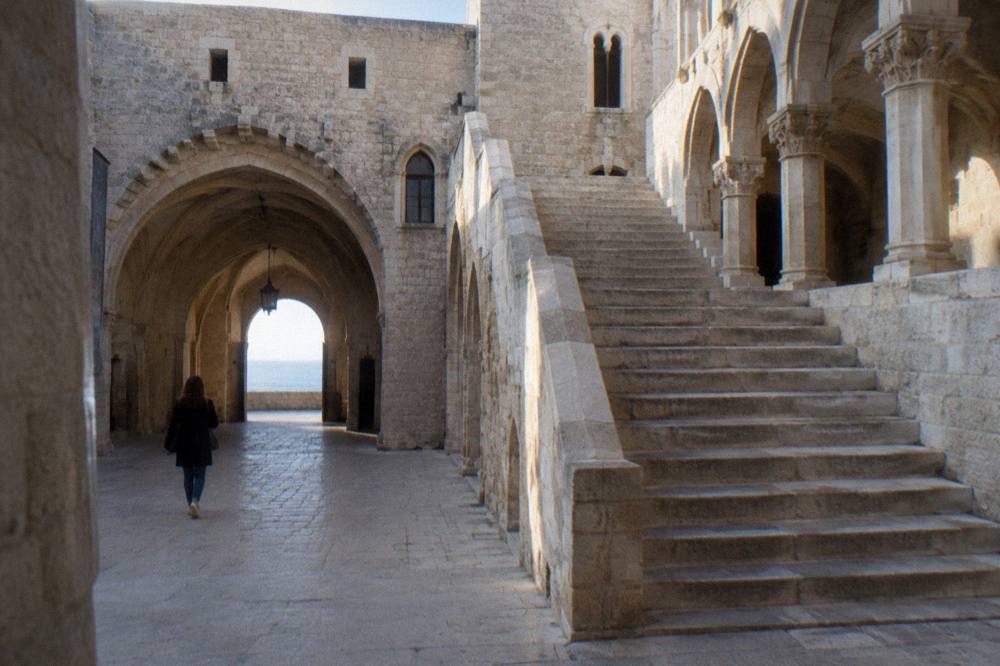 Inner courtyard of a medieval castle with a pale stone arcade, a broad staircase and a vaulted passage