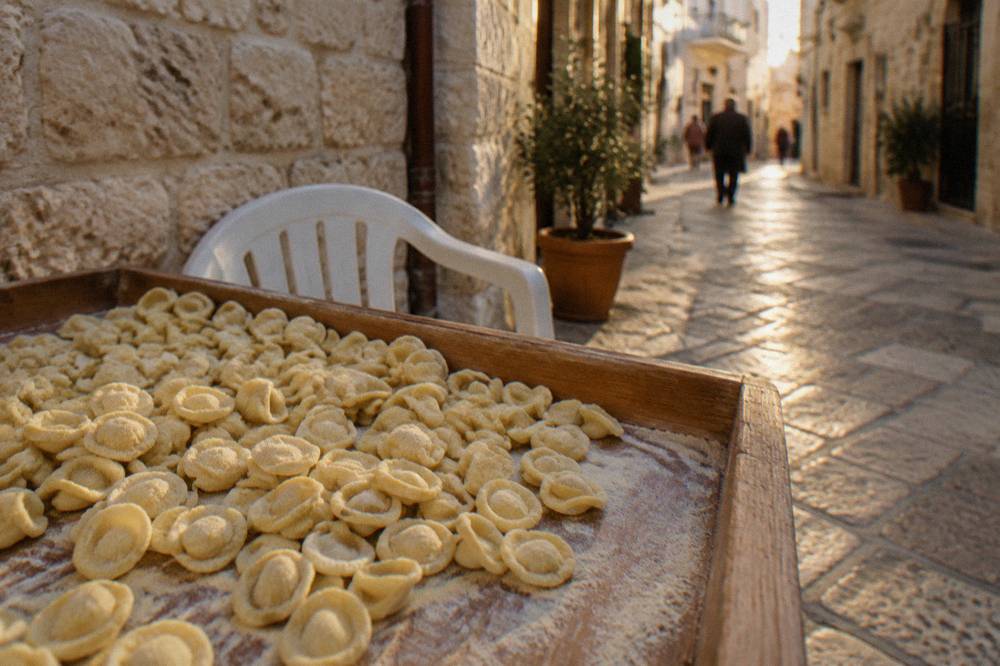 Tray of small ear-shaped orecchiette dusted with semolina on a wooden table beside a plastic chair