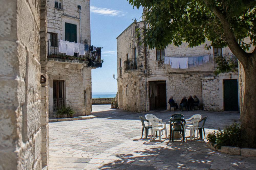 Tiny square where plastic chairs are drawn up in a circle and elderly residents chat far off in the shade