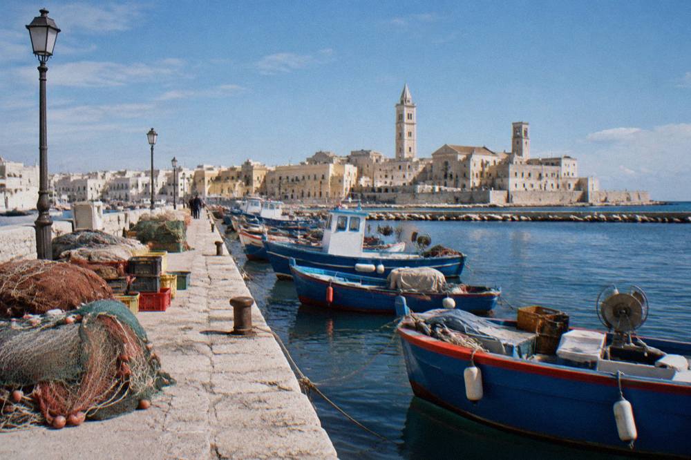 Old harbour pier with small wooden fishing boats, crates and nets and the pale old town skyline with two towers behind