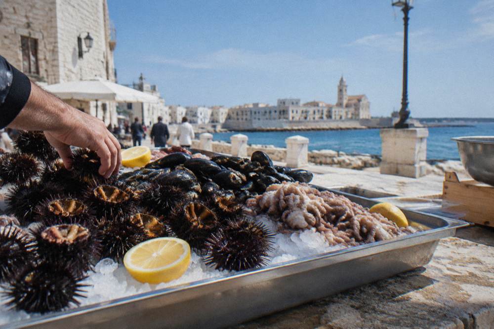 Fresh sea urchins, mussels and small octopus on crushed ice with lemon halves on a stone market counter