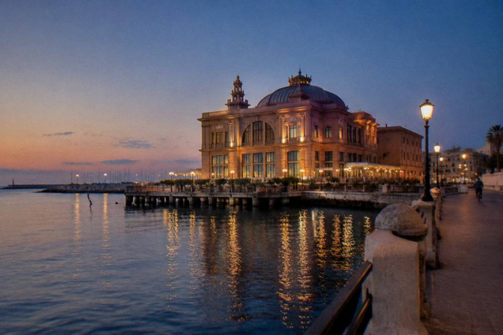 Waterside Liberty-style building at dusk with soft light on its decorated facade and still harbour water