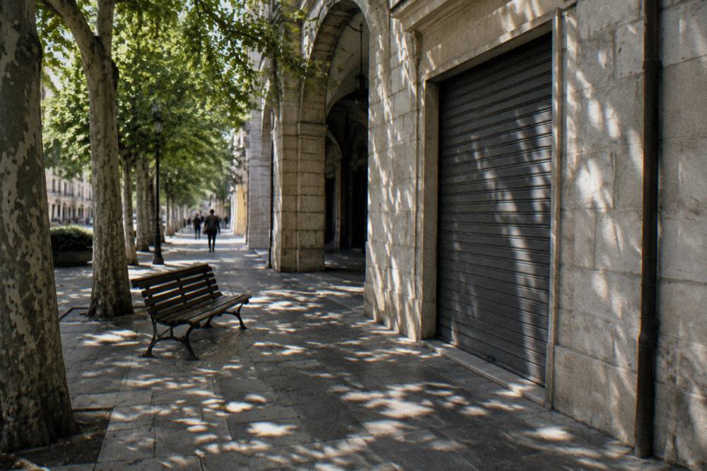 Shaded corner of a district with a cream stone shopfront, a bench and dappled light