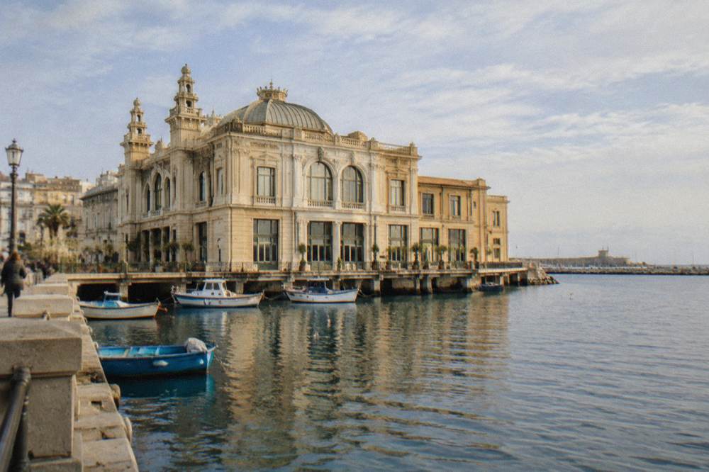 Ornate Liberty-style building standing at the edge of harbour water with boats beside it