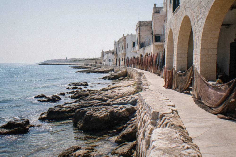 Rocky shore beside simple seafront houses with nets drying in hazy morning light