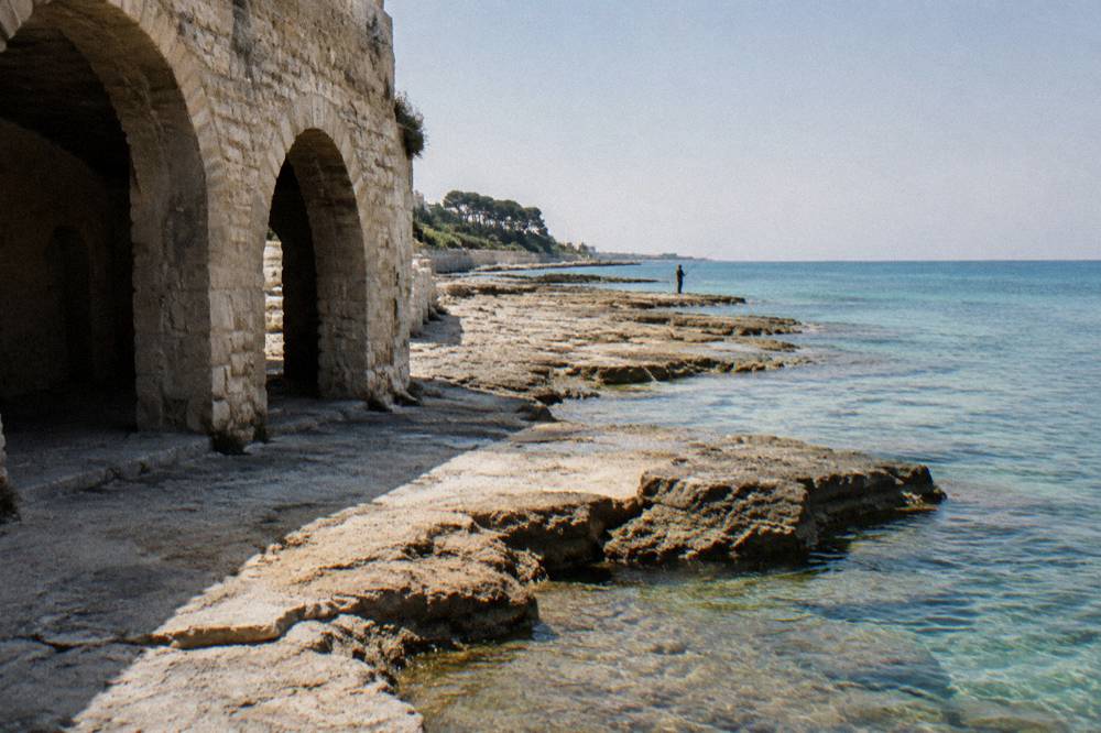 Flat limestone rock shelves running into clear shallow water with a distant angler in low sun