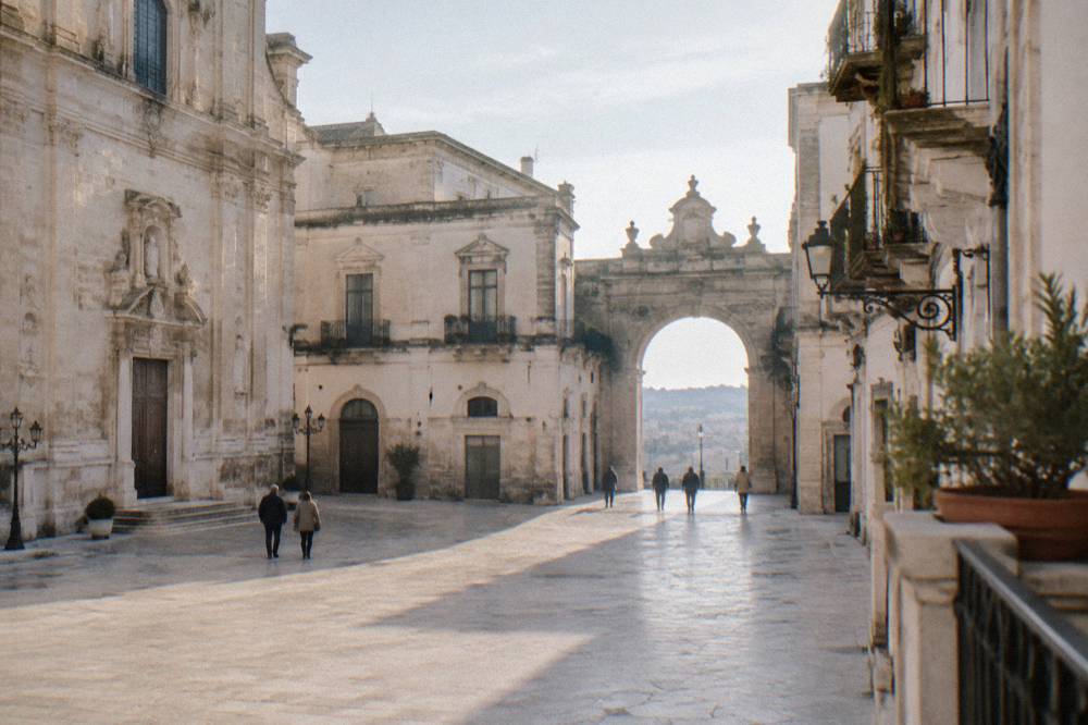 Baroque town square with cream and white facades, wrought-iron balconies and an arched gateway