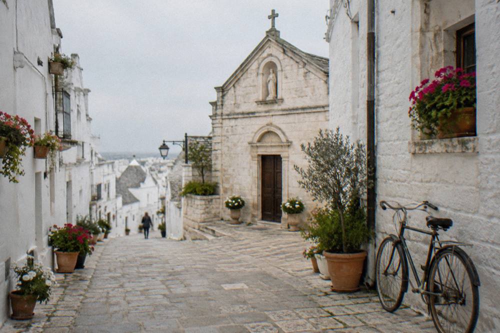 White lane with flower pots, a tiny church front and a bicycle leaning on the wall