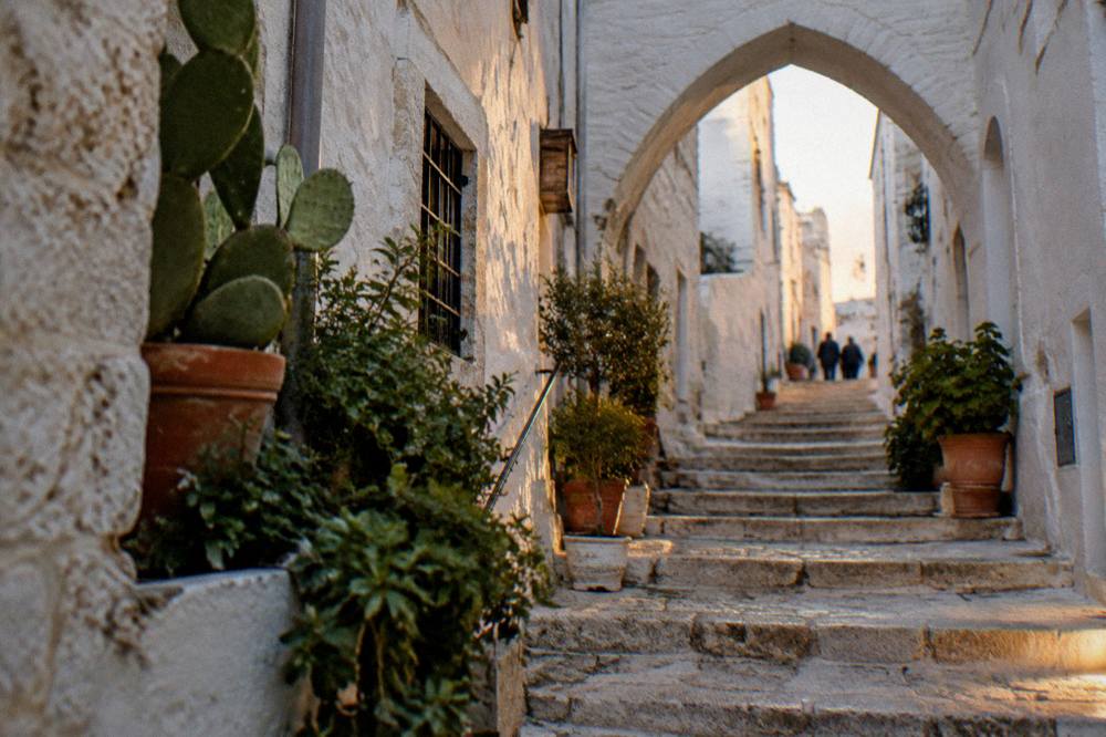 Steep whitewashed alley with stone steps, a pointed arch overhead and potted plants