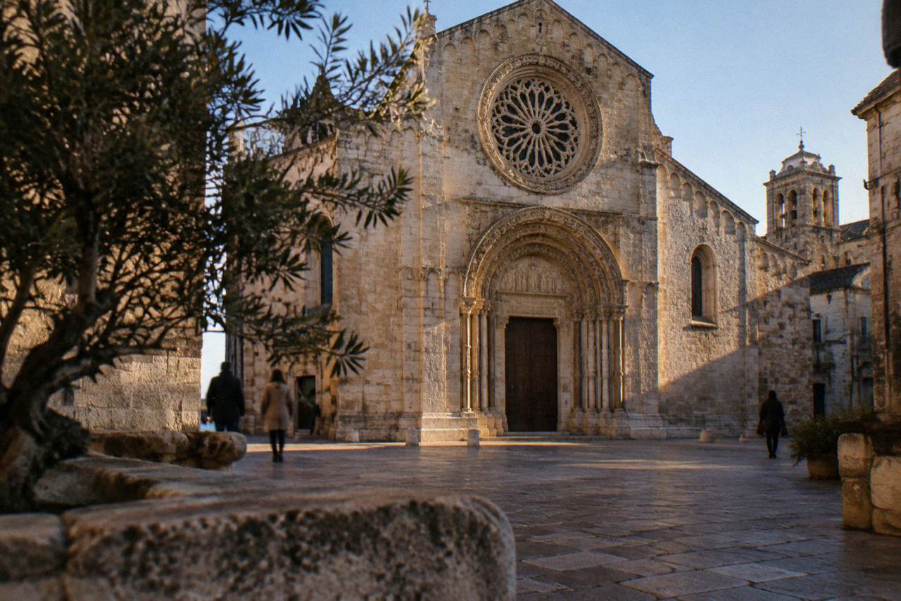 Romanesque cathedral in warm limestone with a carved rose window and portal on a small square