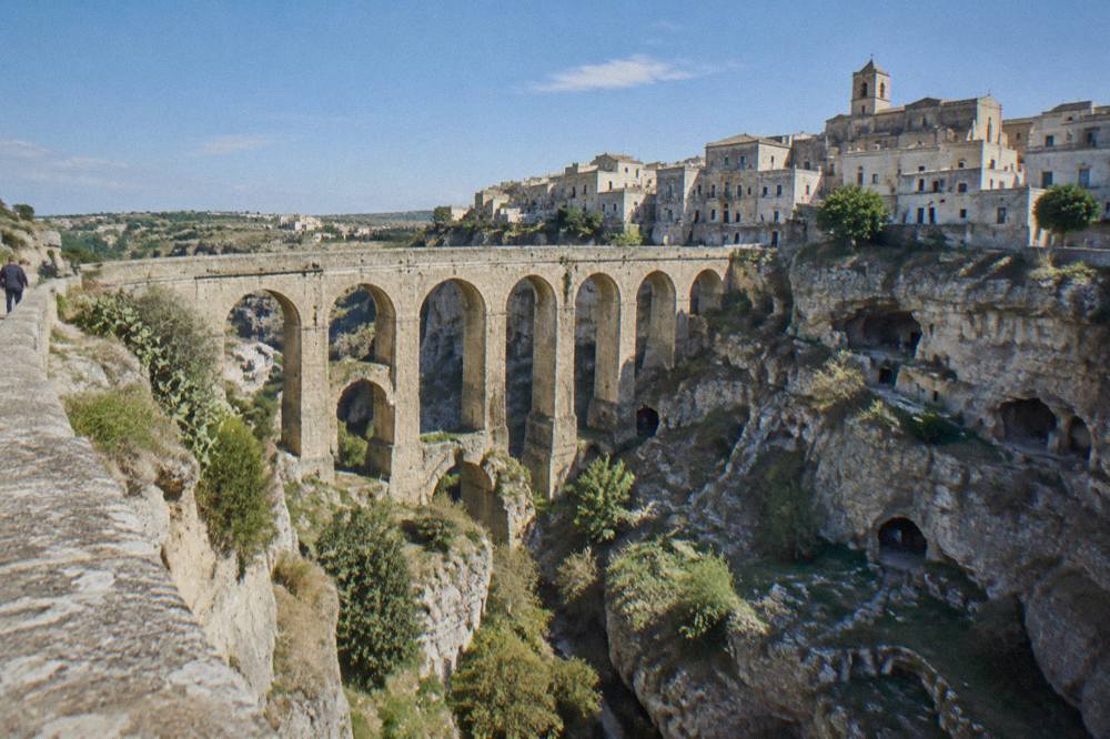 Deep rocky ravine crossed by a tall many-arched stone bridge with old town houses on the far rim
