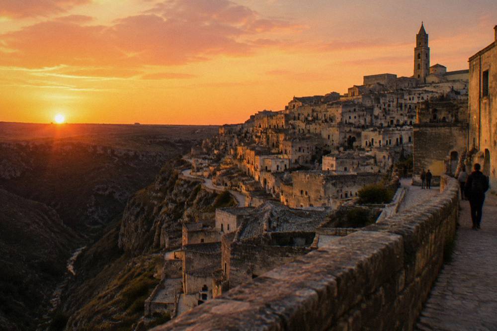 Sunset gold on stacked rooftops and cave facades of an ancient stone town above a shadowed ravine