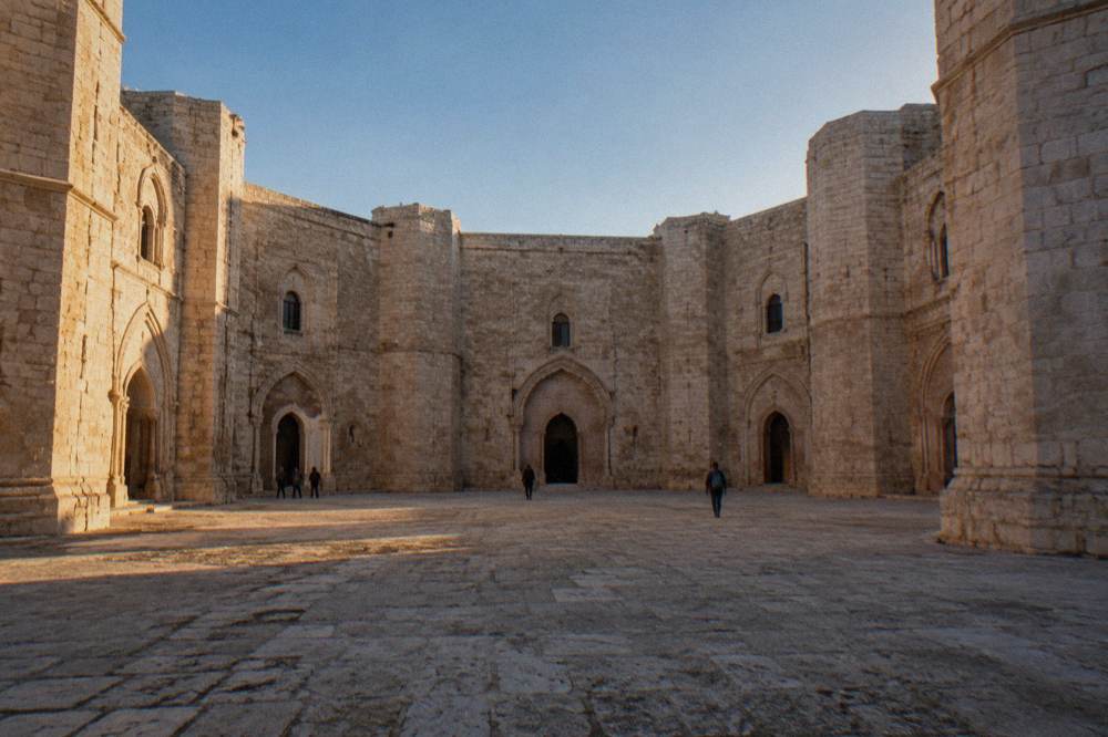 Octagonal inner courtyard of a medieval castle with arched doorways in pale stone and a blue sky