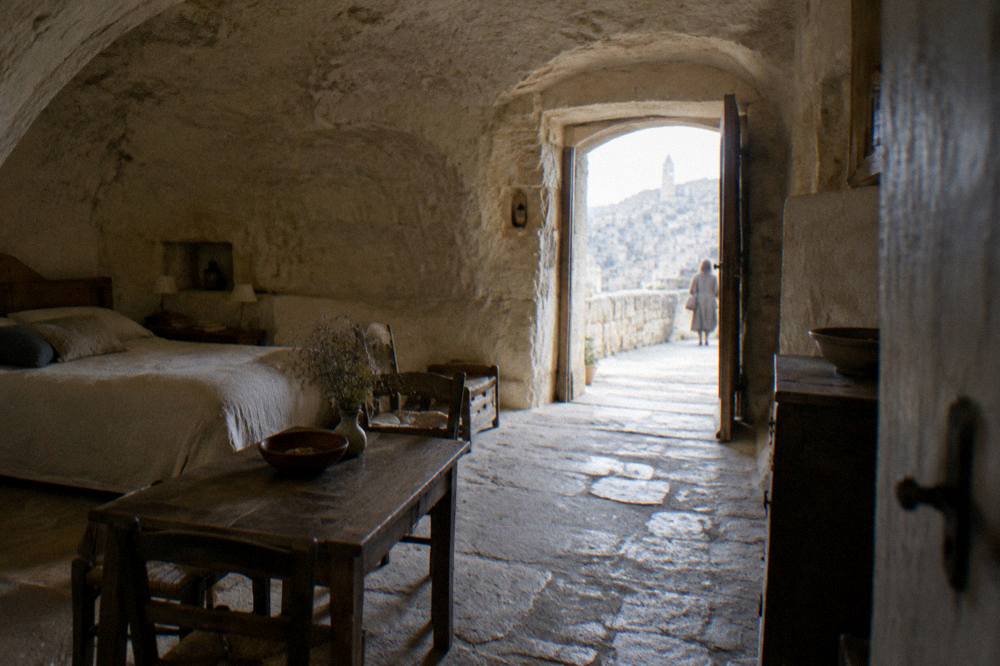 Inside a restored cave dwelling with an arched rock ceiling, a simple bed and a wooden table