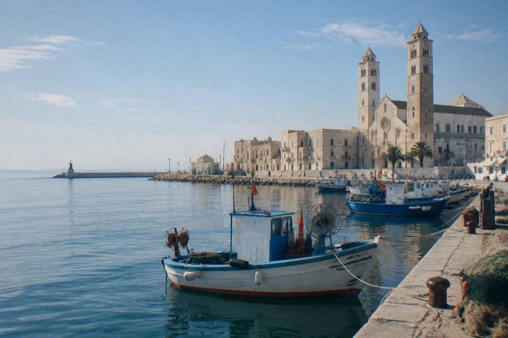 Old harbour with fishing boats at the quay and a twin-towered Romanesque cathedral near the shore