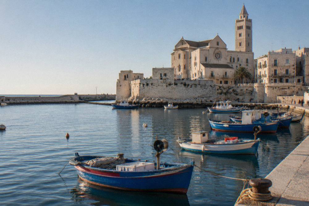 Small harbour town with old fishing boats in a stone-walled inlet and a pale stone cathedral behind