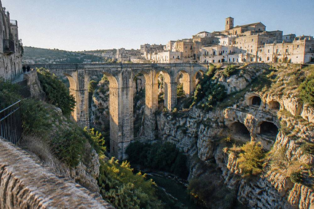 Deep rocky ravine crossed by a tall many-arched stone bridge with old town houses on the far rim