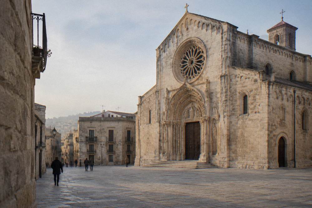 Romanesque cathedral in warm limestone with a carved rose window and portal on a small square