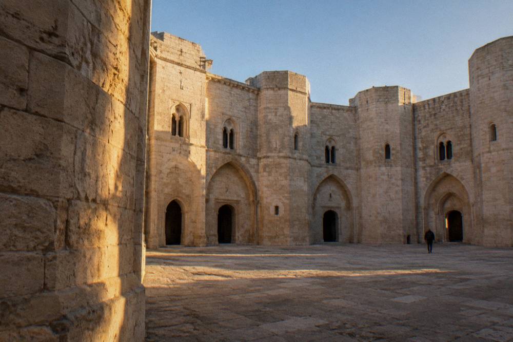 Octagonal inner courtyard of a medieval castle with arched doorways in pale stone and a blue sky