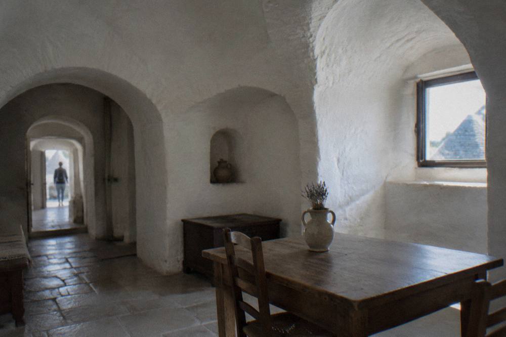 Whitewashed domed room with deep arched alcoves, a simple wooden table and a ceramic jug